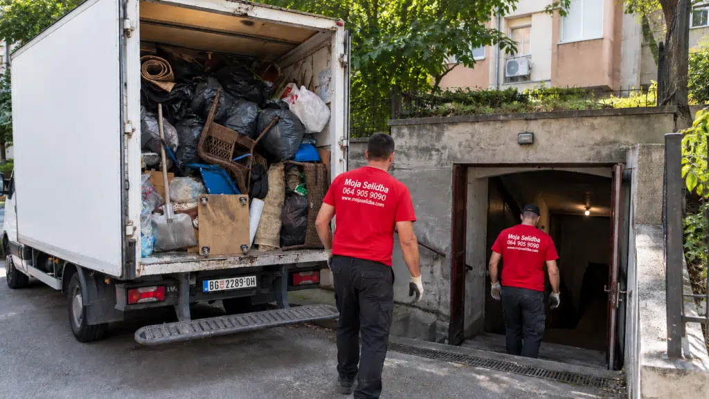 Radnici u crvenim majicama iznose stare stvari iz podruma pored kamiona za odvoz