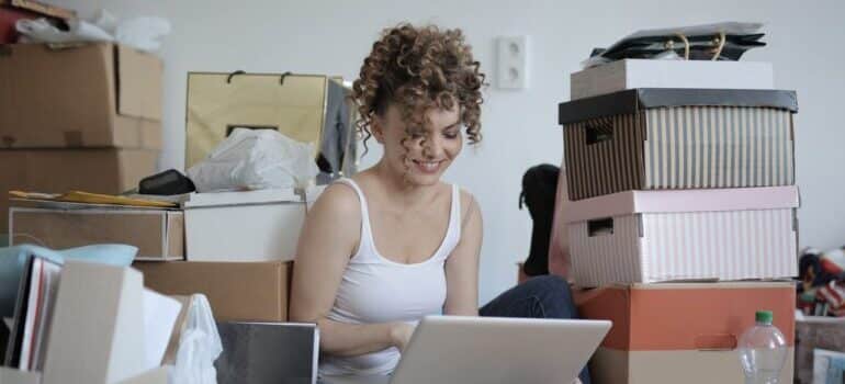 devojka sa laptopom koja sedi među kutijama